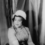 Black and white photo of a woman sitting and wearing a hat